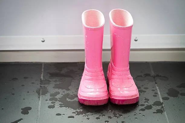 Pair of pink rain boots placed on a wet tile floor