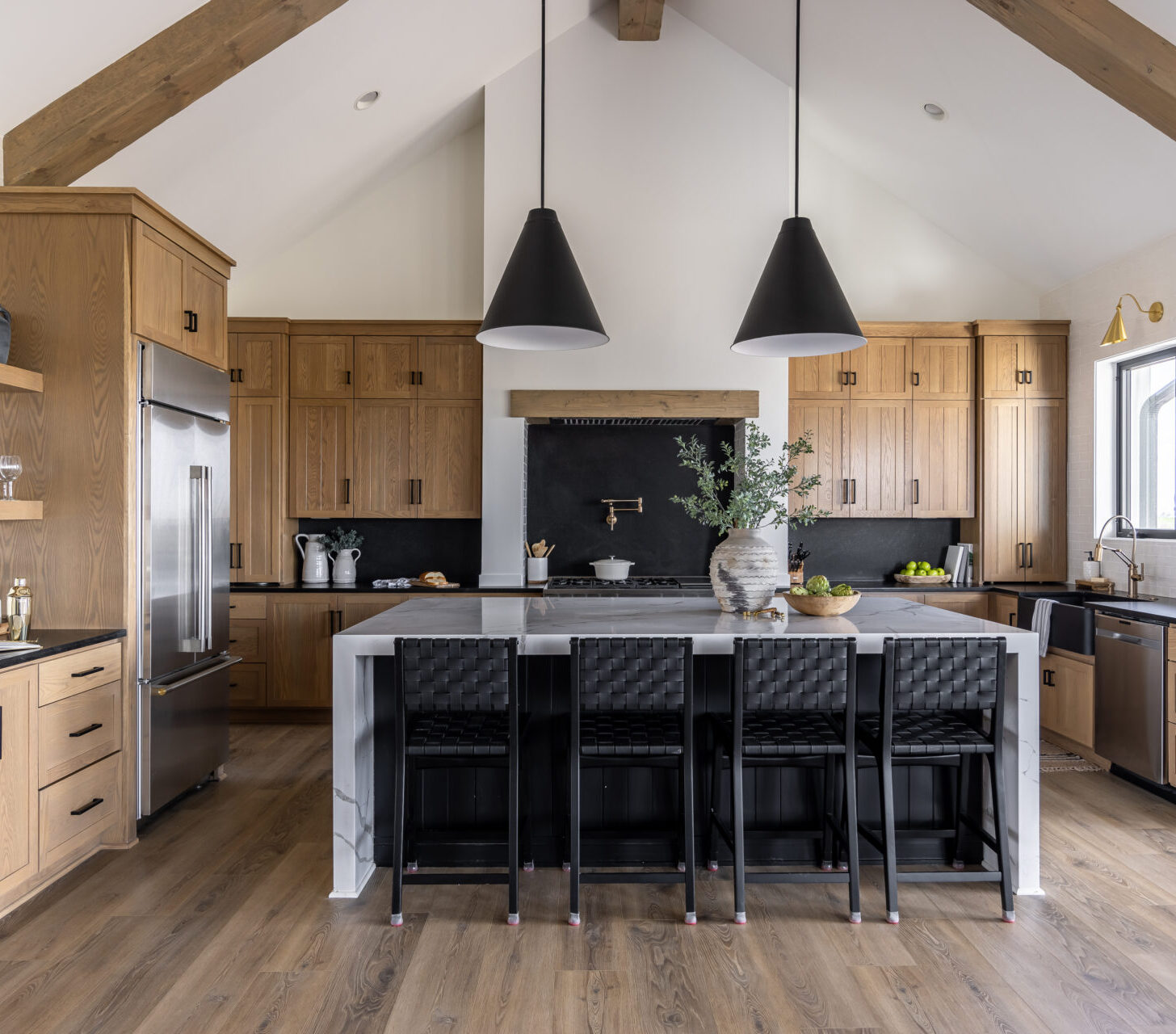 Modern kitchen with wood cabinets, large island with black chairs, and stainless steel appliances, showcasing available cabinetry at the Billings, MT location.